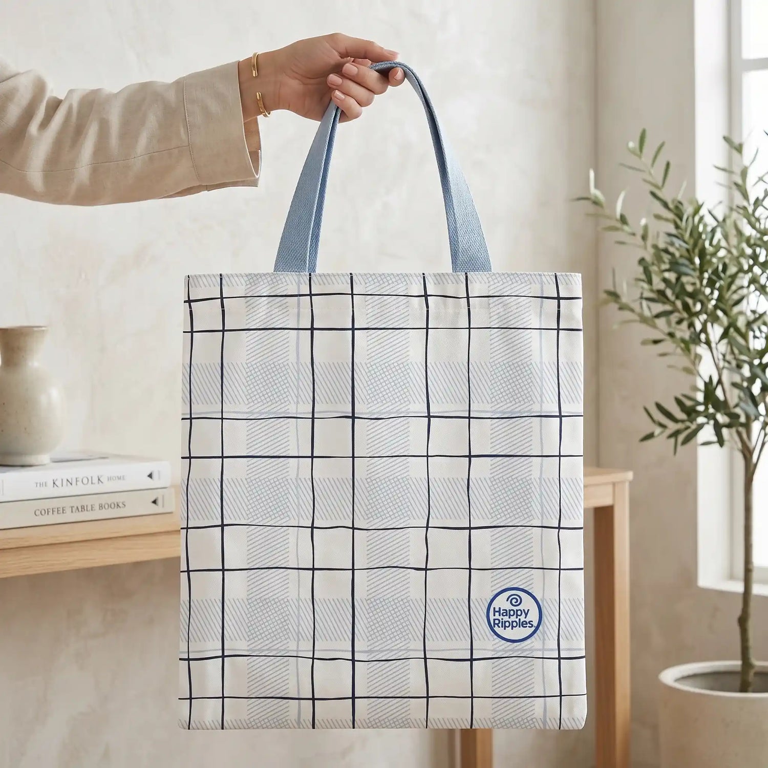 Happy Ripples plaid tote bag held by hand in a minimalist home setting.
