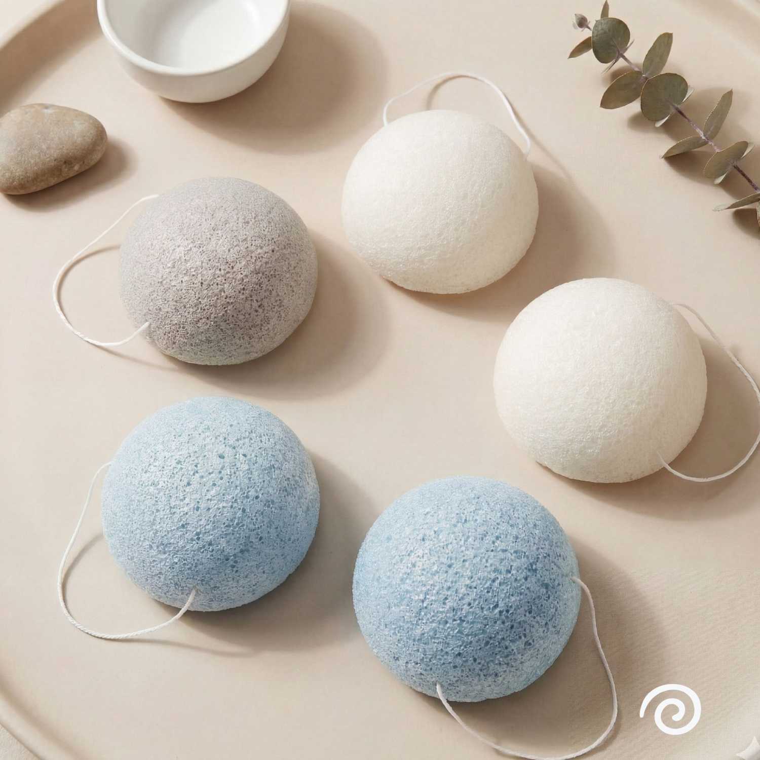 Happy Ripples Konjac facial sponges in blue white and gray arranged on a neutral tray with eucalyptus and soft spa styling